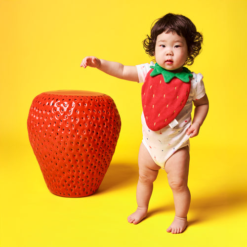 Bib-A-Deez Strawberry Drool Bib worn by standing baby, standing next to strawberry sculpture