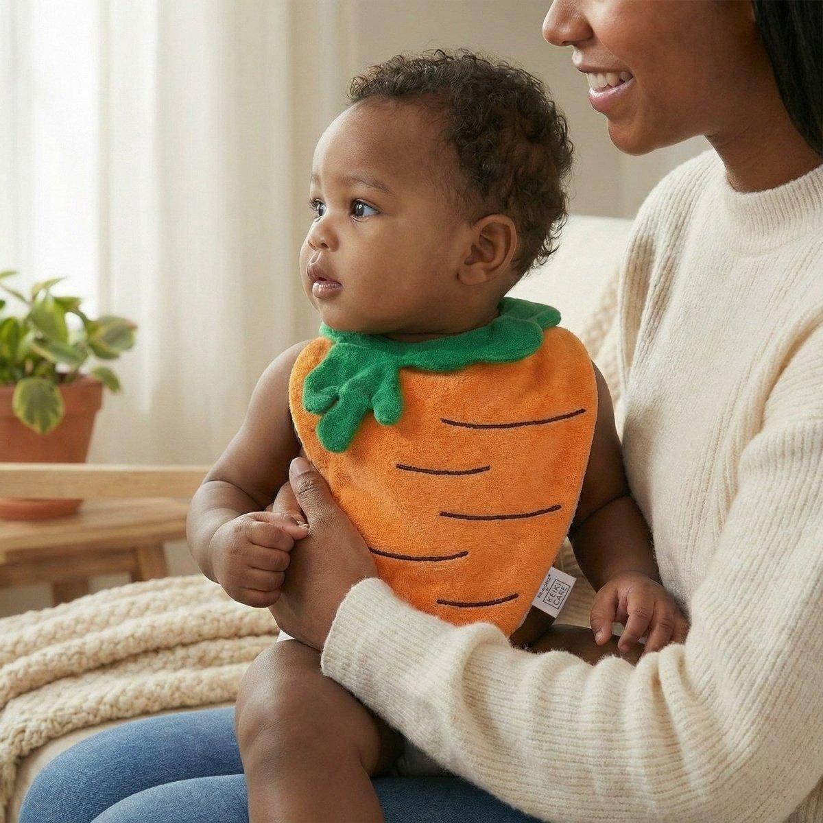 mom holding baby wearing bright carrot-shaped bib, playful lifestyle image